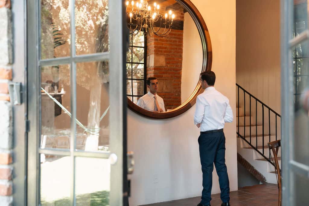 Groom adjusting his tie in front of the mirror