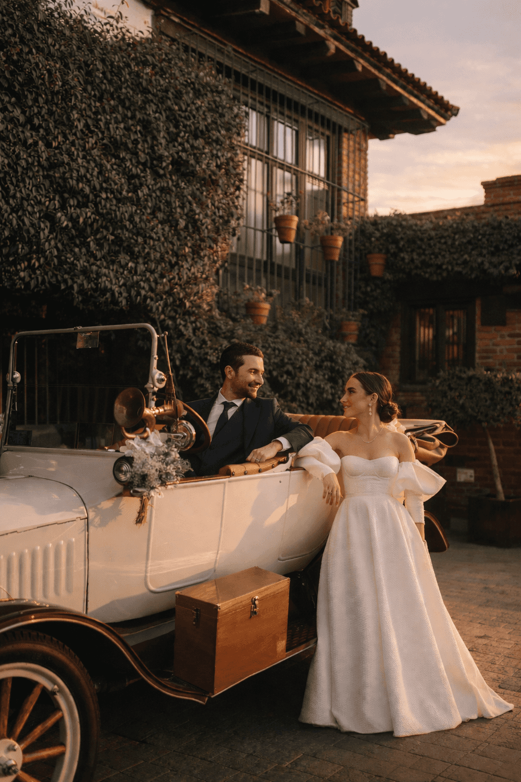 Bride and groom by the classic car in front of the hacienda facade at dusk