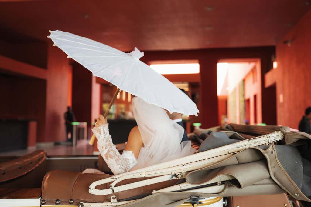 Bride with umbrella in classic car in front of the red facade